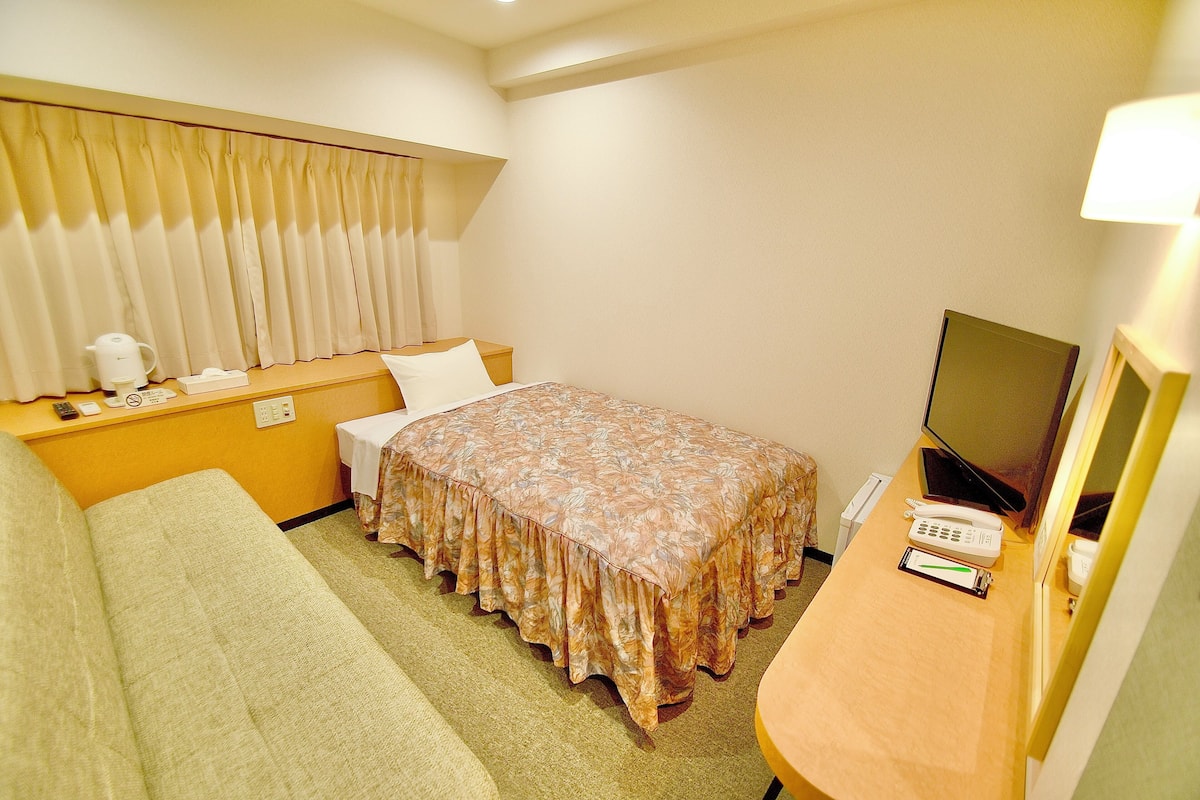 Habitación de hotel con cama, sofá, televisión y escritorio con teléfono y lámpara.