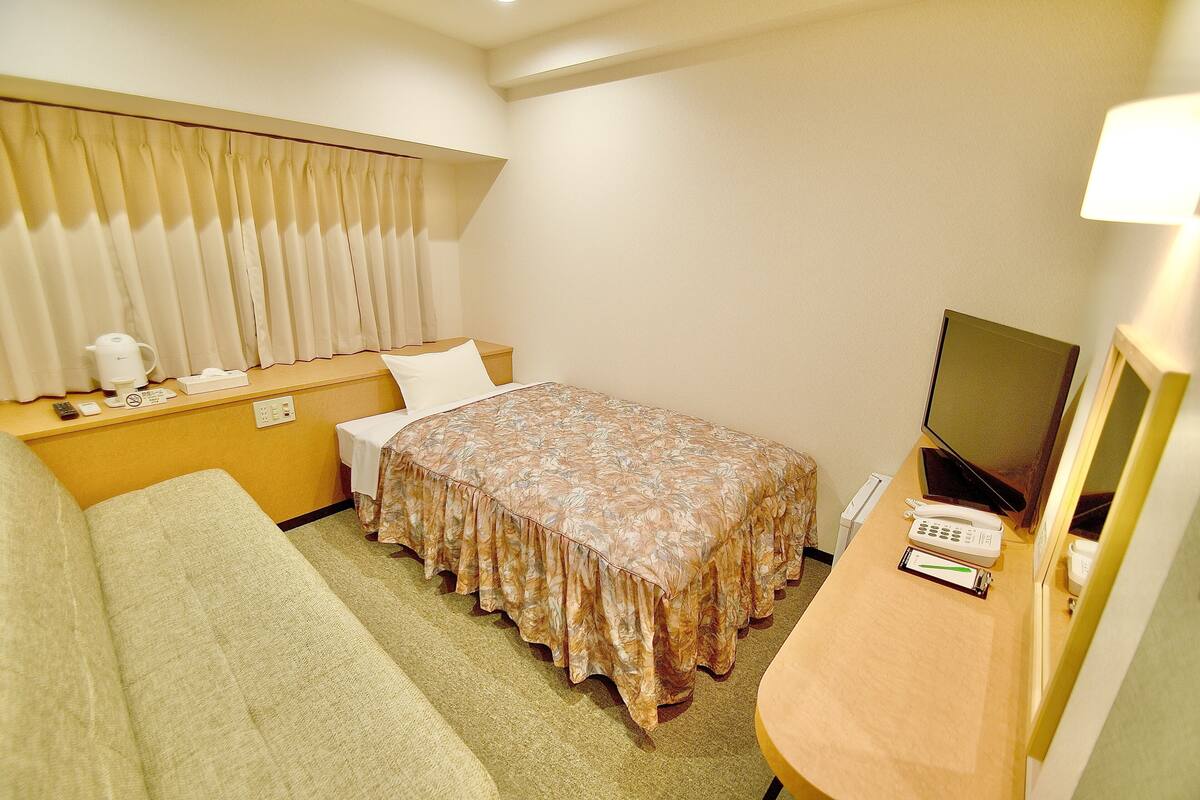 Habitación de hotel con cama, sofá, televisión y escritorio con teléfono y lámpara.