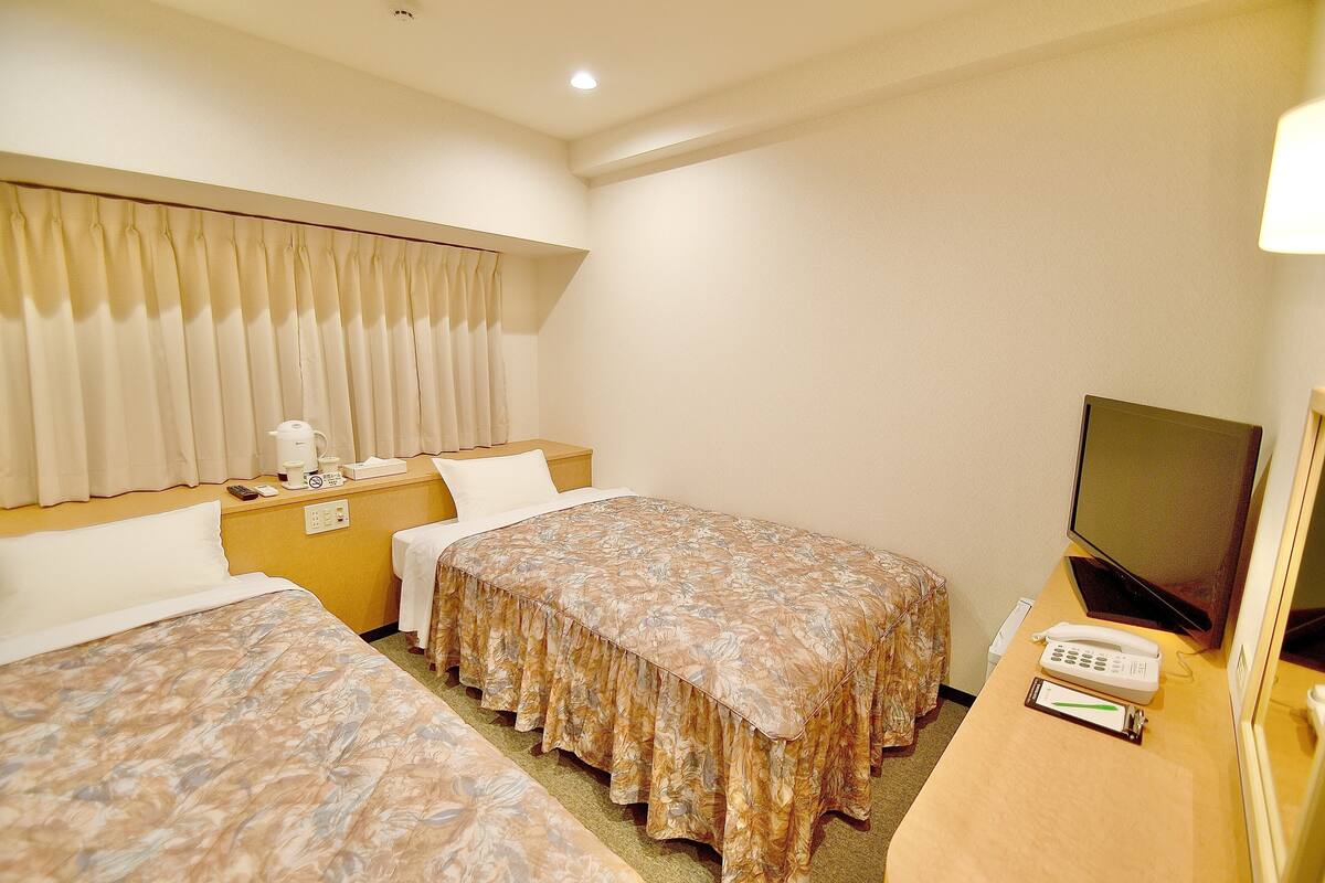 Una habitación de hotel con dos camas, televisión, teléfono y mesita de noche.