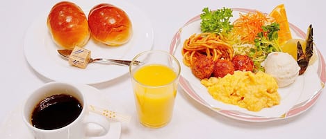 A breakfast setting with two rolls, a cup of coffee, a glass of orange juice, and a plate with scrambled eggs, meatballs, spaghetti, and vegetables.