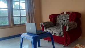 A room with a red armchair, a blue stool with a laptop, and a window with curtains. - SPOT ON 93596 Pondok Wisata Pesona Asri (Pleret)