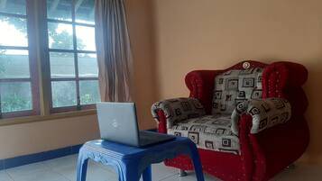 A room with a red armchair, a blue stool with a laptop, and a window with curtains.