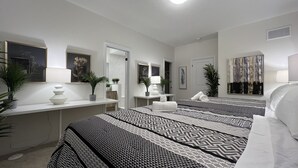 Ein Hotelzimmer mit einem großen Bett, einem Schreibtisch und einem Stuhl. Zimmerpflanzen und Kunstwerke schmücken die Wände.