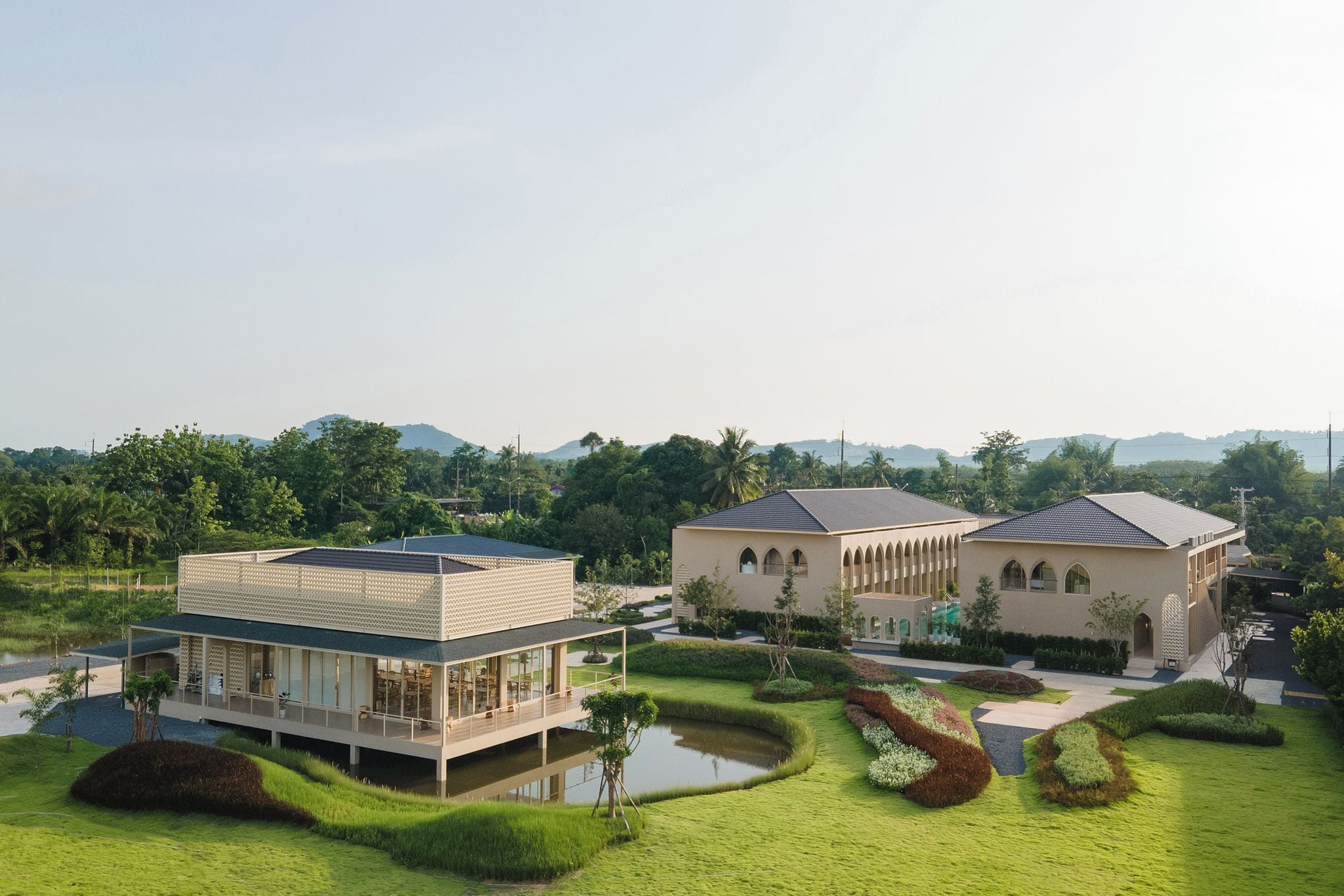 Un edificio moderno con tetto piatto e ampia facciata vetrata, immerso in giardini curati e affacciato su uno specchio d'acqua.