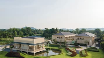 Un bâtiment moderne doté d’un toit plat et d’une grande façade vitrée, entouré de jardins bien entretenus et bordé par un plan d’eau.