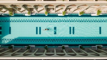 Una piscina con agua cristalina, una persona nadando y sillas de descanso junto a la piscina.