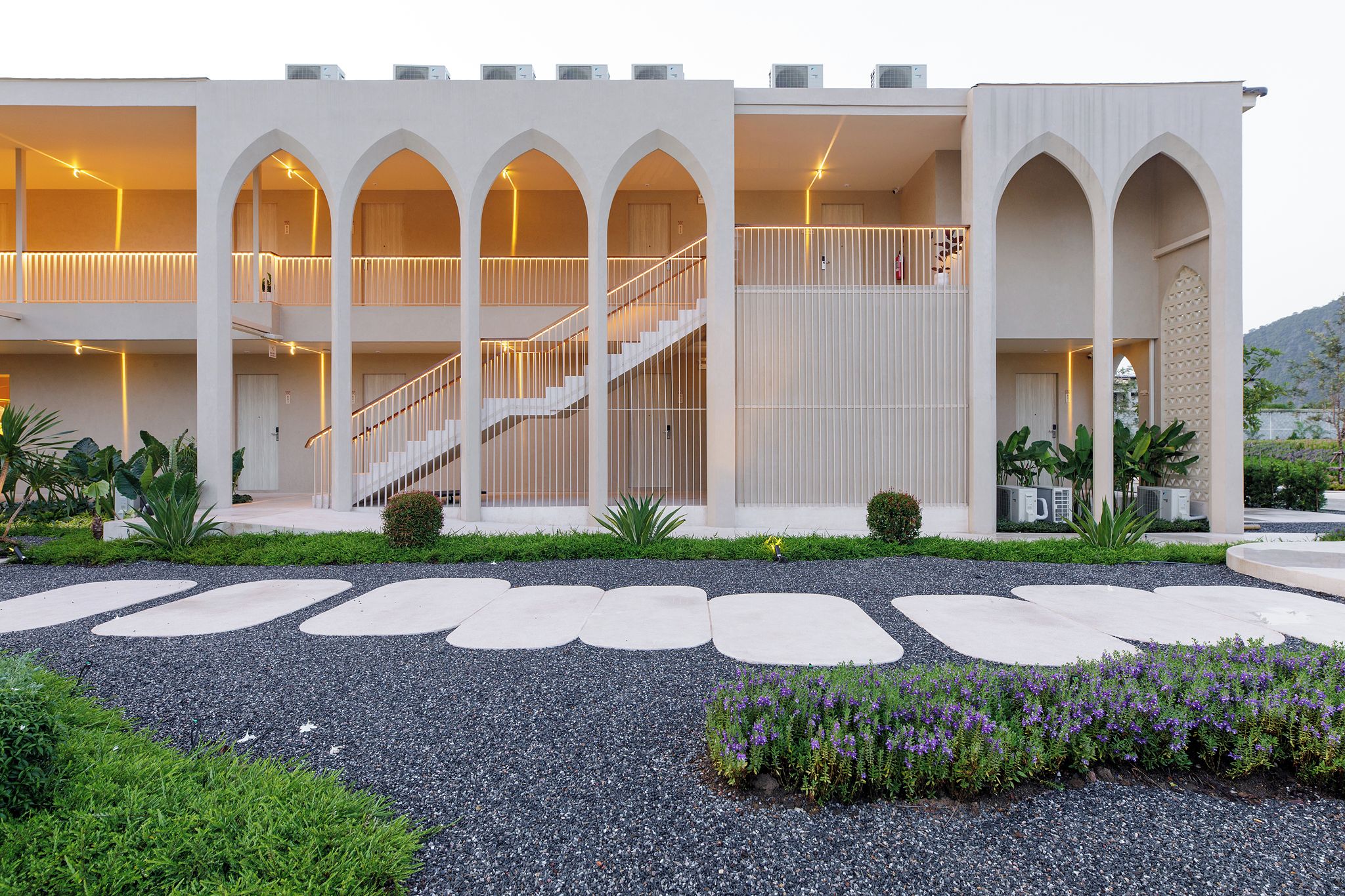 A modern building with multiple balconies, a central staircase, and a landscaped garden area.