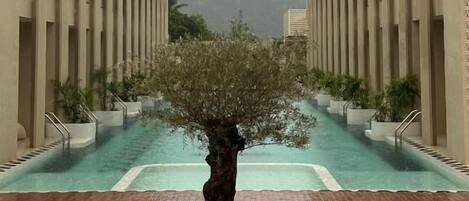 A pool area with a central tree, surrounded by arched walkways and a view of misty mountains.