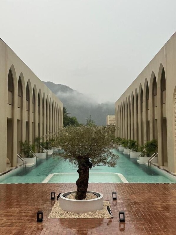 A pool area with a central tree, surrounded by arched walkways and a view of misty mountains. - Navakiri Boutique Resort Satun (Satun)