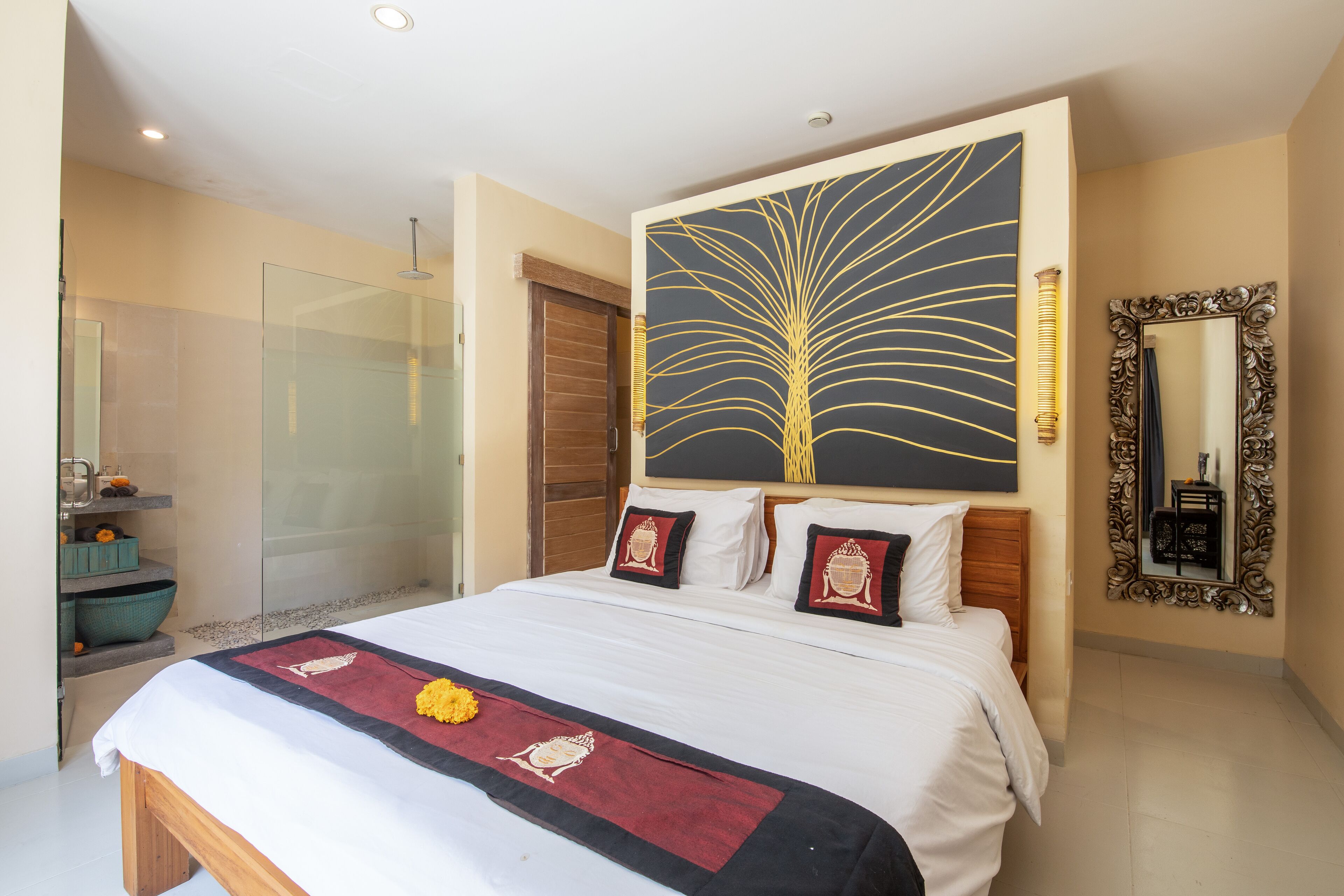 A hotel room with a large bed, a glass shower enclosure, a decorative wall painting, and a mirror with an ornate frame.