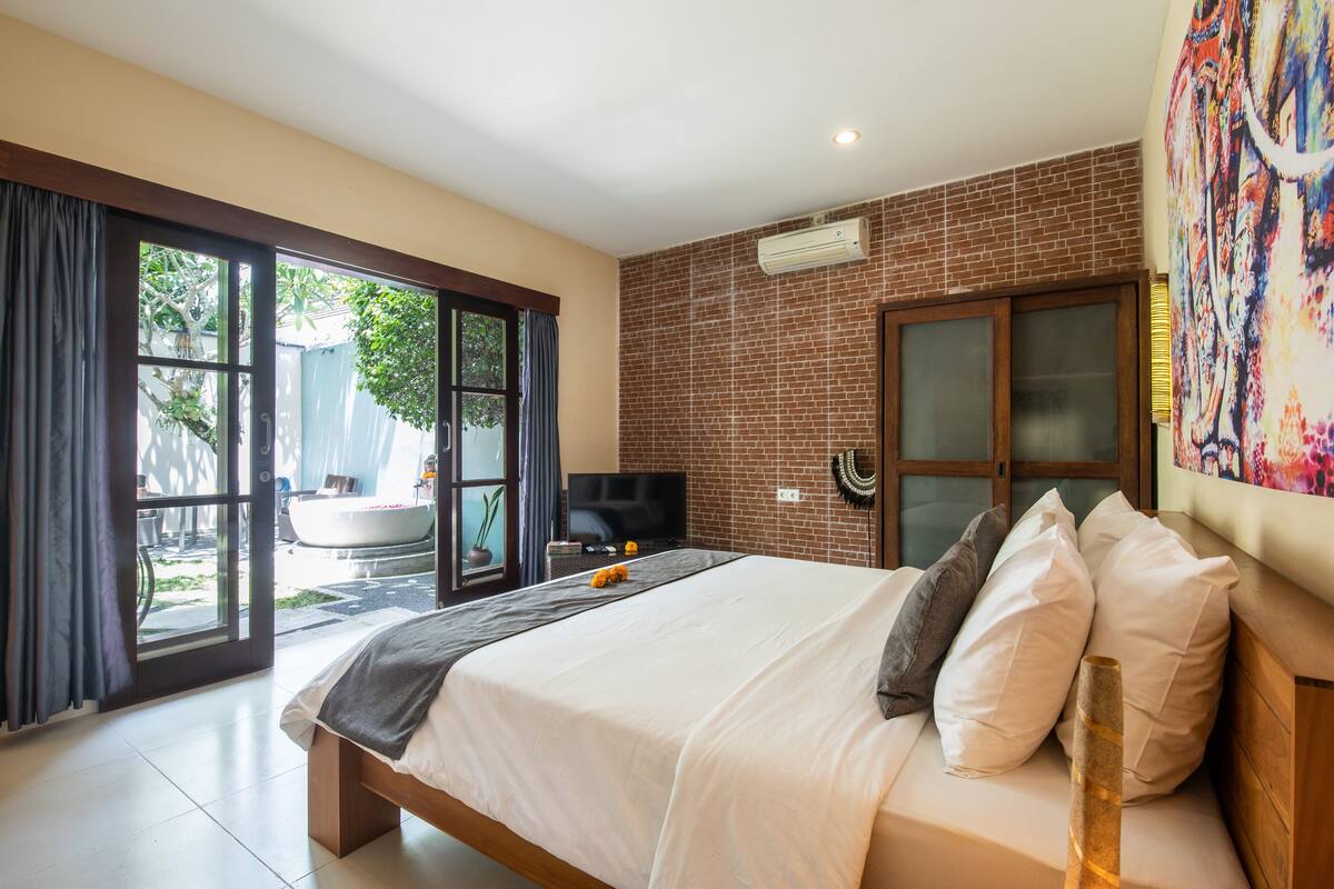 A modern hotel room with a large bed, a television, and a view of the outdoor area.