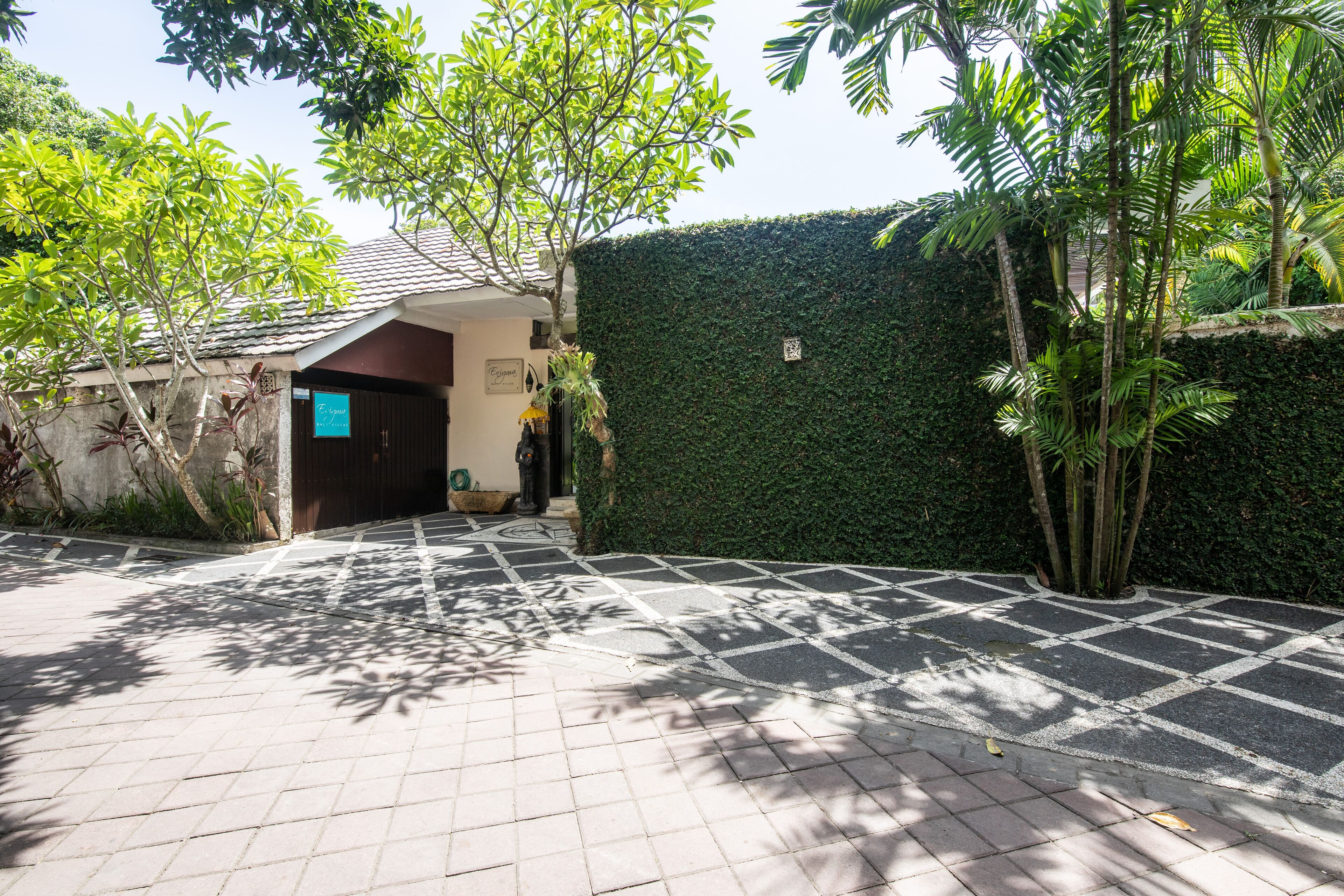 A paved pathway leading to a building with a tiled roof and a green hedge.