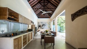 A modern kitchen with a dining area, featuring a ceiling fan, wooden cabinets, and a view to the outdoors. - Enigma Bali Villas (Canggu)
