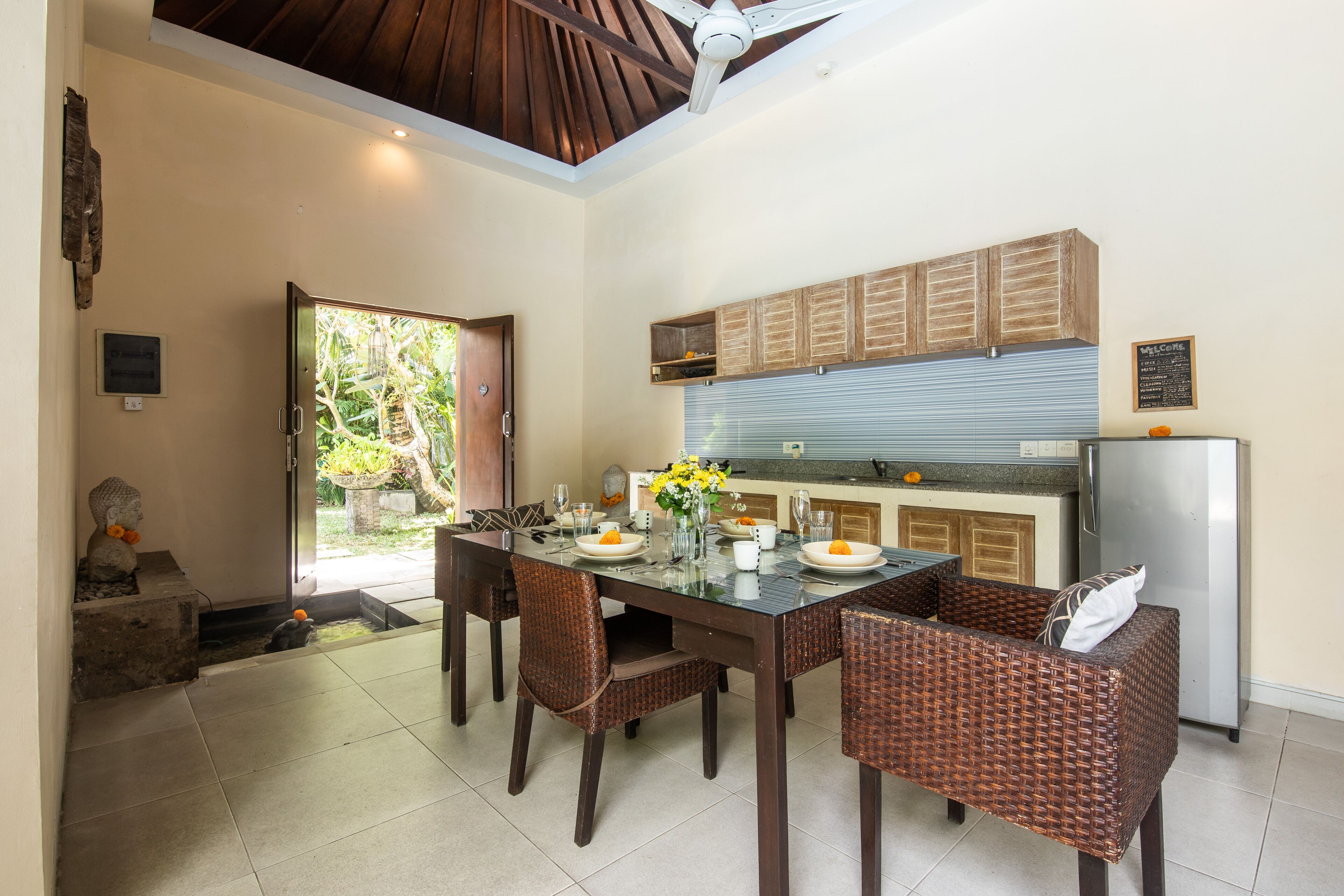 A dining area with a glass table, wicker chairs, and a kitchen in the background.
