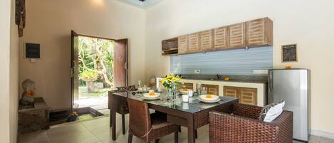 A dining area with a glass table, wicker chairs, and a kitchen in the background.