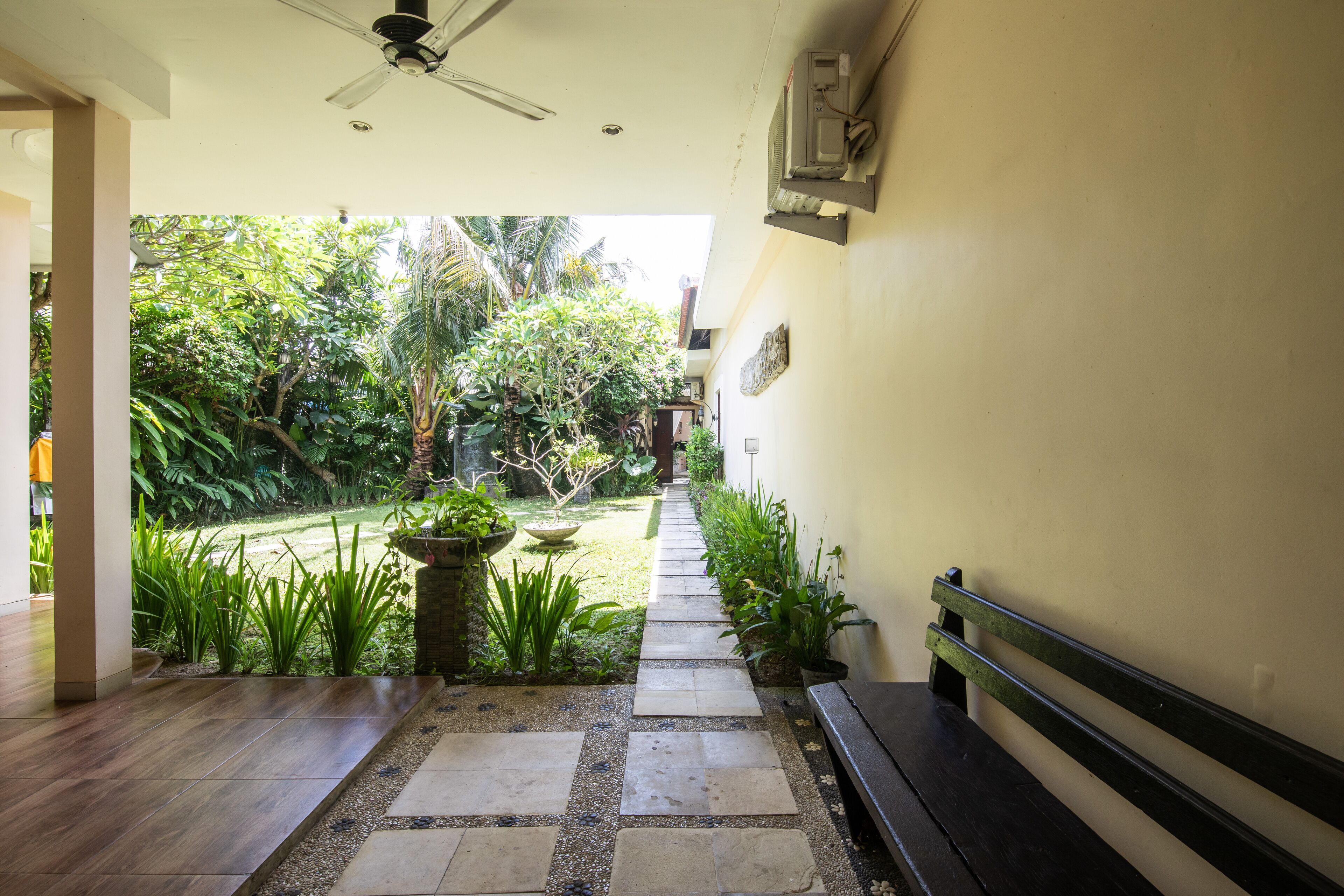 A pathway leading to a garden with a bench and a ceiling fan.
