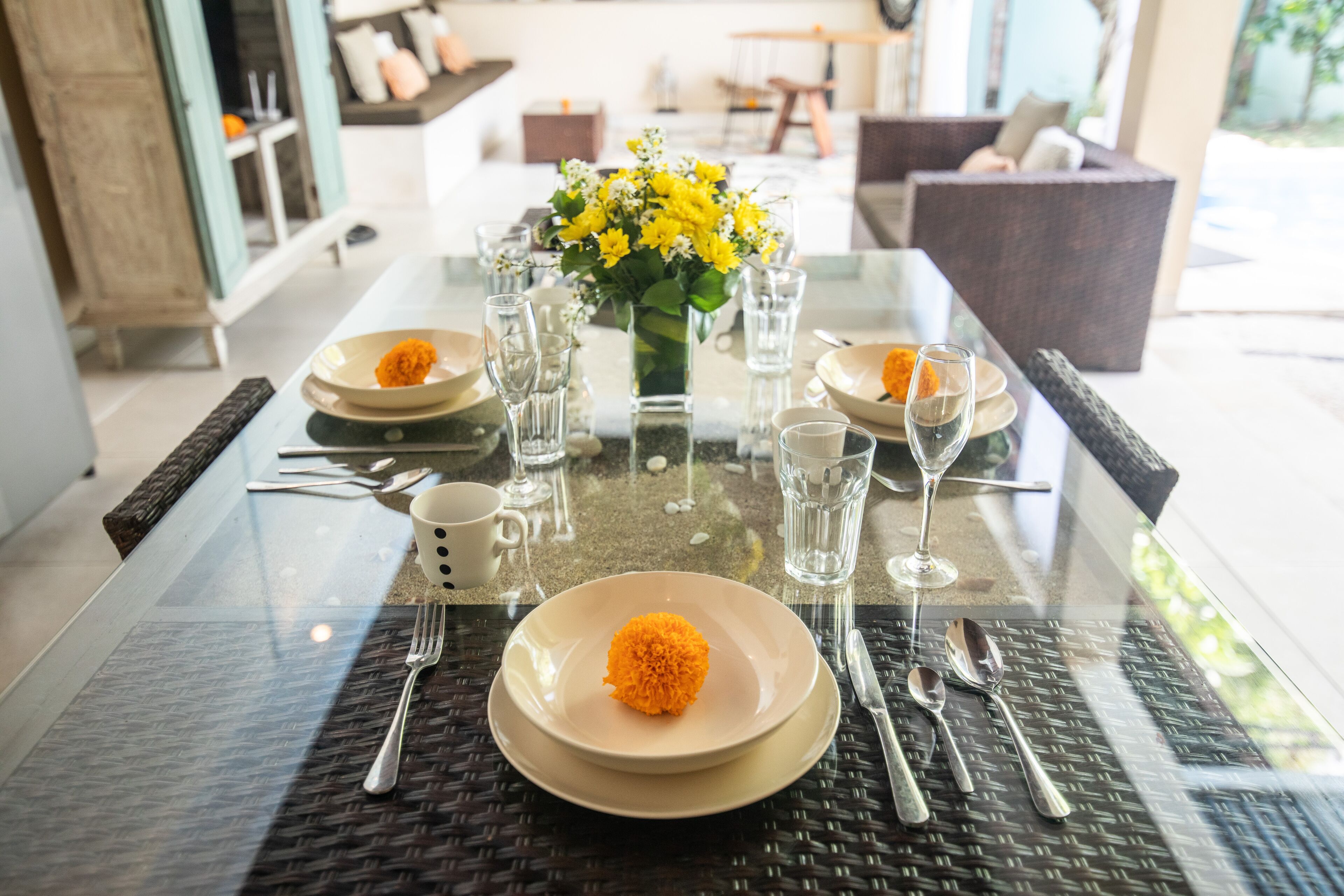 A dining table set with plates, cutlery, and a vase of yellow flowers.