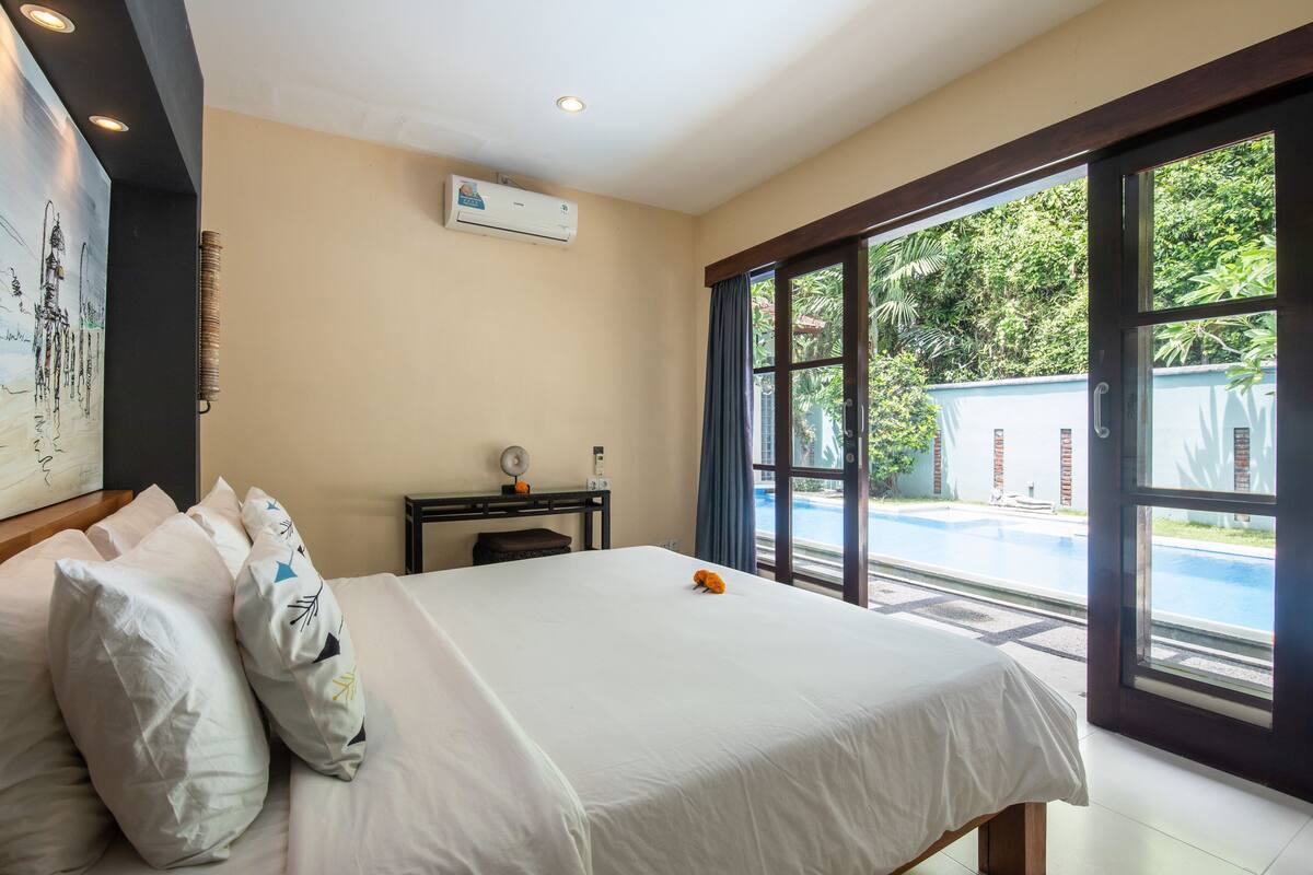 A hotel room with a large bed, a desk, and a view of an outdoor swimming pool.