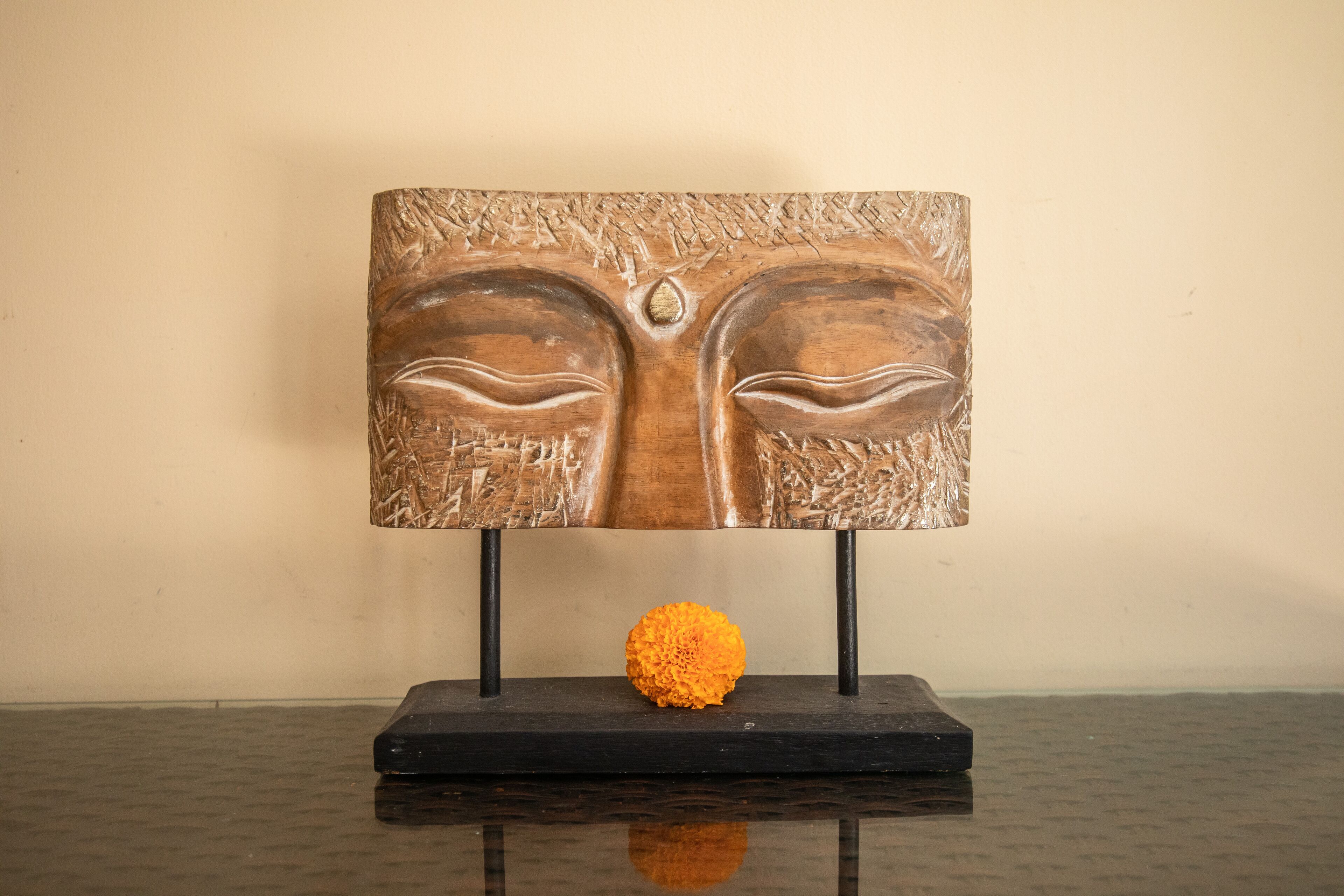 A wooden sculpture with a textured surface and a single orange flower on a black stand.