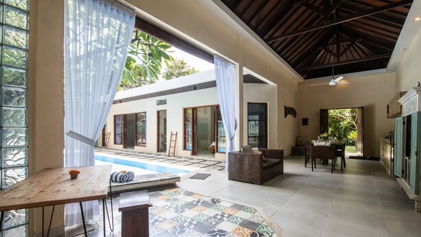 A spacious indoor area with a pool, a dining area, and a seating area with a view of the outdoors. - Enigma Bali Villas (Canggu)