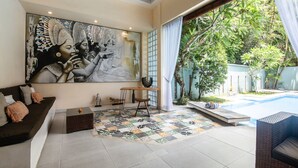 A modern living room with a large abstract painting, a sofa, a coffee table, and a view of a swimming pool and greenery. - Enigma Bali Villas (Canggu)