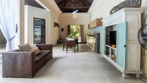 A spacious living area with a high ceiling, a dining table, and a kitchen area with a fan. - Enigma Bali Villas (Canggu)