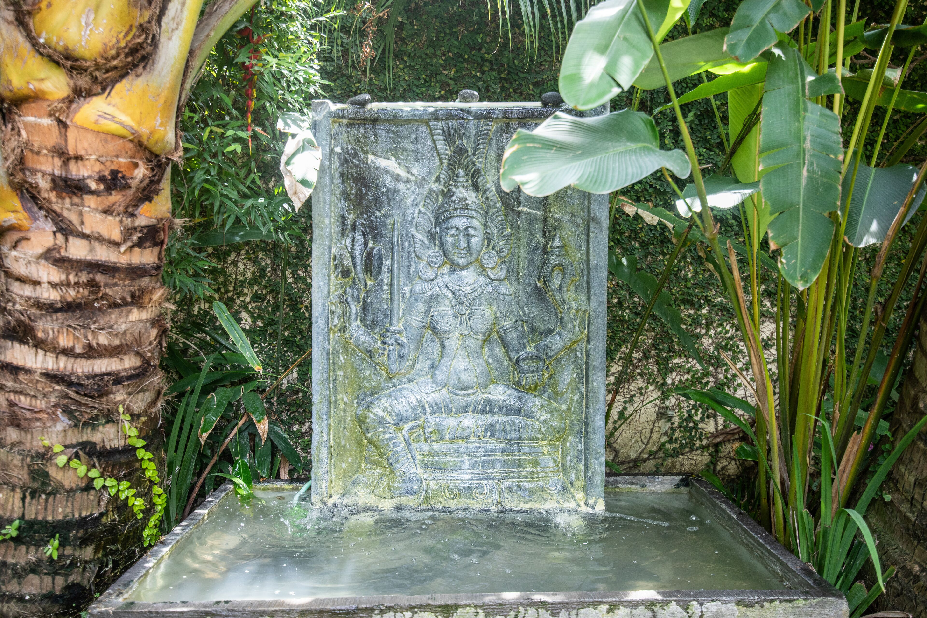 Una statua in pietra raffigura una figura seduta su un piedistallo, circondata da vegetazione lussureggiante.