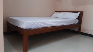 Uma cama de solteiro com estrutura de madeira e roupa de cama branca em um quarto com paredes lisas e chão de azulejos.