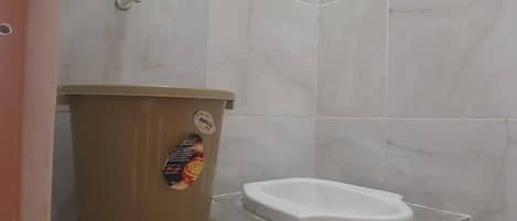 Et badeværelse med toilet, skraldespand og vandhane.