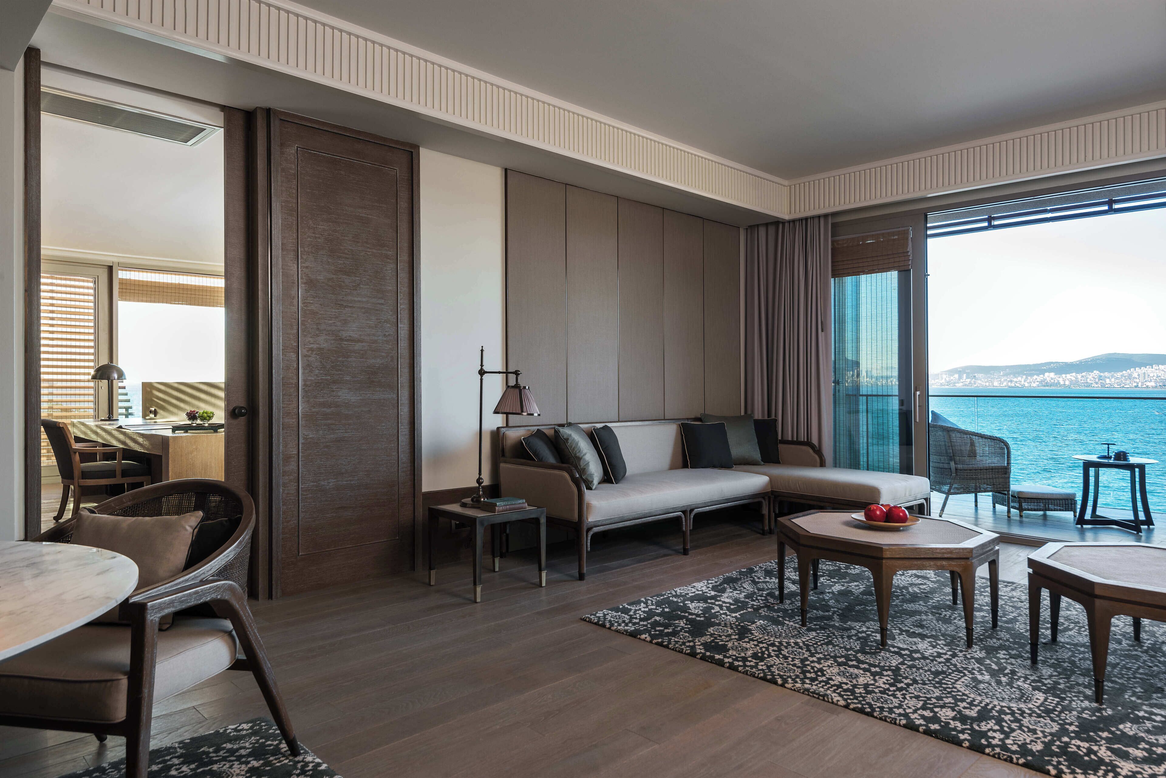 Una sala moderna con sofá, mesa de centro y sillas, un comedor con mesa y sillas, y un ventanal con vista al mar.