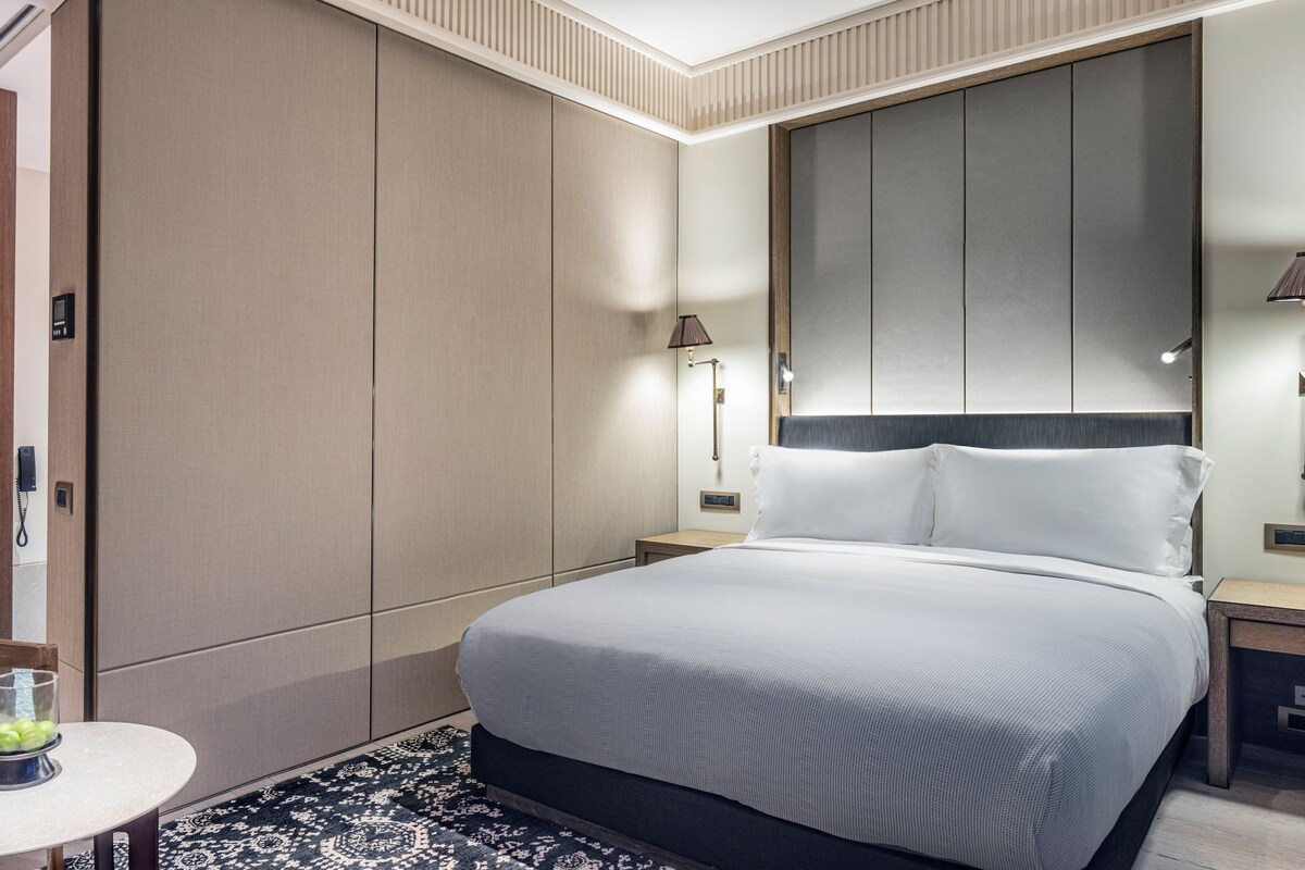 A hotel room with a bed, bedside tables, a chair, a small table with a glass, and a wardrobe.
