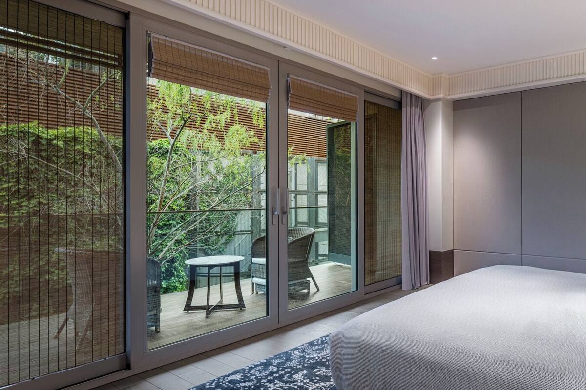 A modern hotel room with a large bed, a glass door leading to an outdoor area, and a view of greenery.