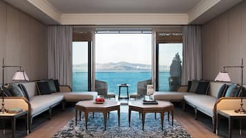 Enjoy a panoramic view of the water and distant hills from the comfort of this stylish room, featuring a sofa set, side tables, and a patterned rug.