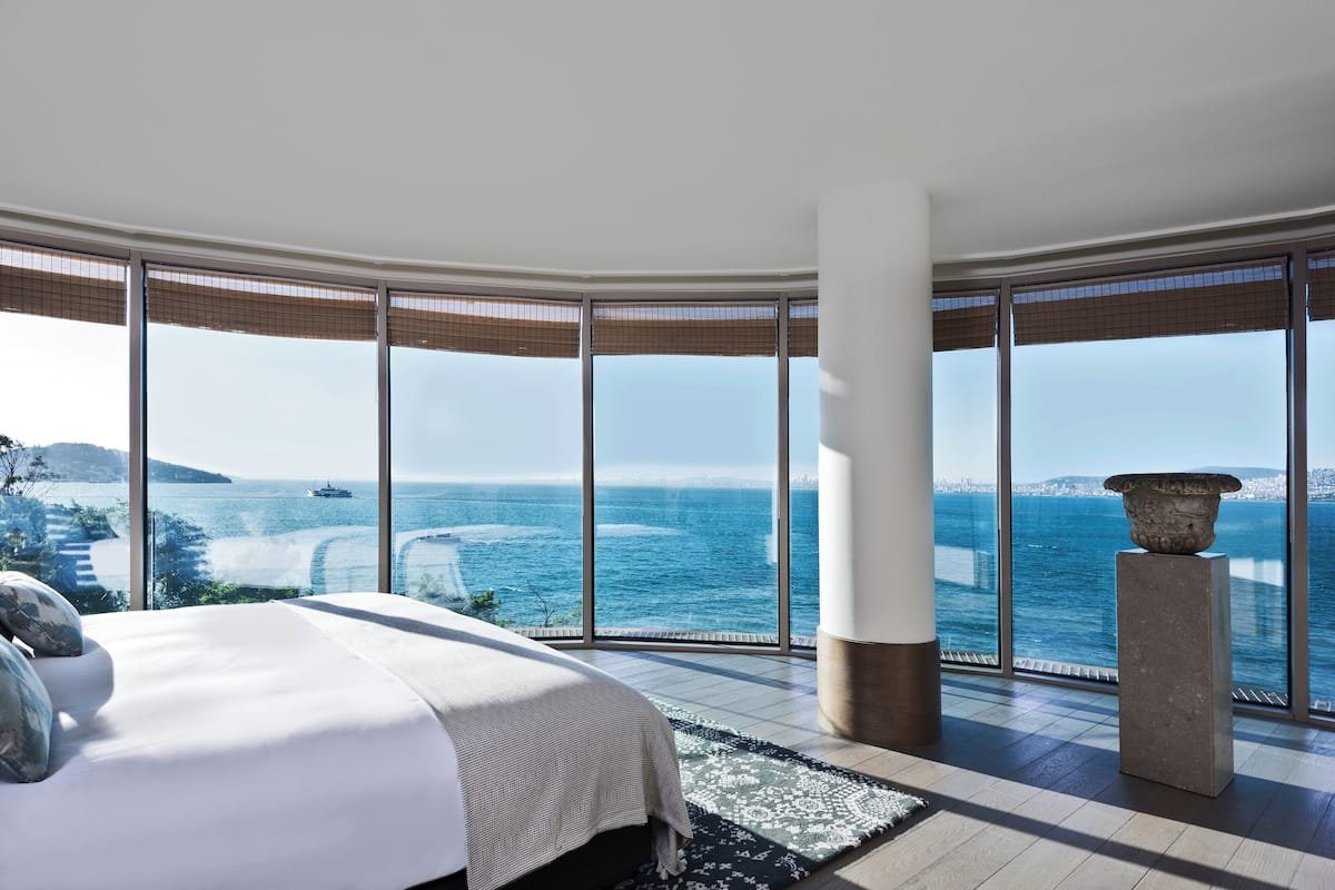 A bedroom with a large bed, a view of the sea, and a stone pillar.