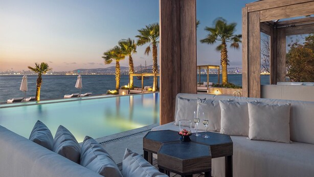 A poolside area with a view of the sea, a sofa, and a table with glasses and a bowl of fruit. - Princes’ Palace Resort - Member of The Leading Hotels of the World (Adalar)