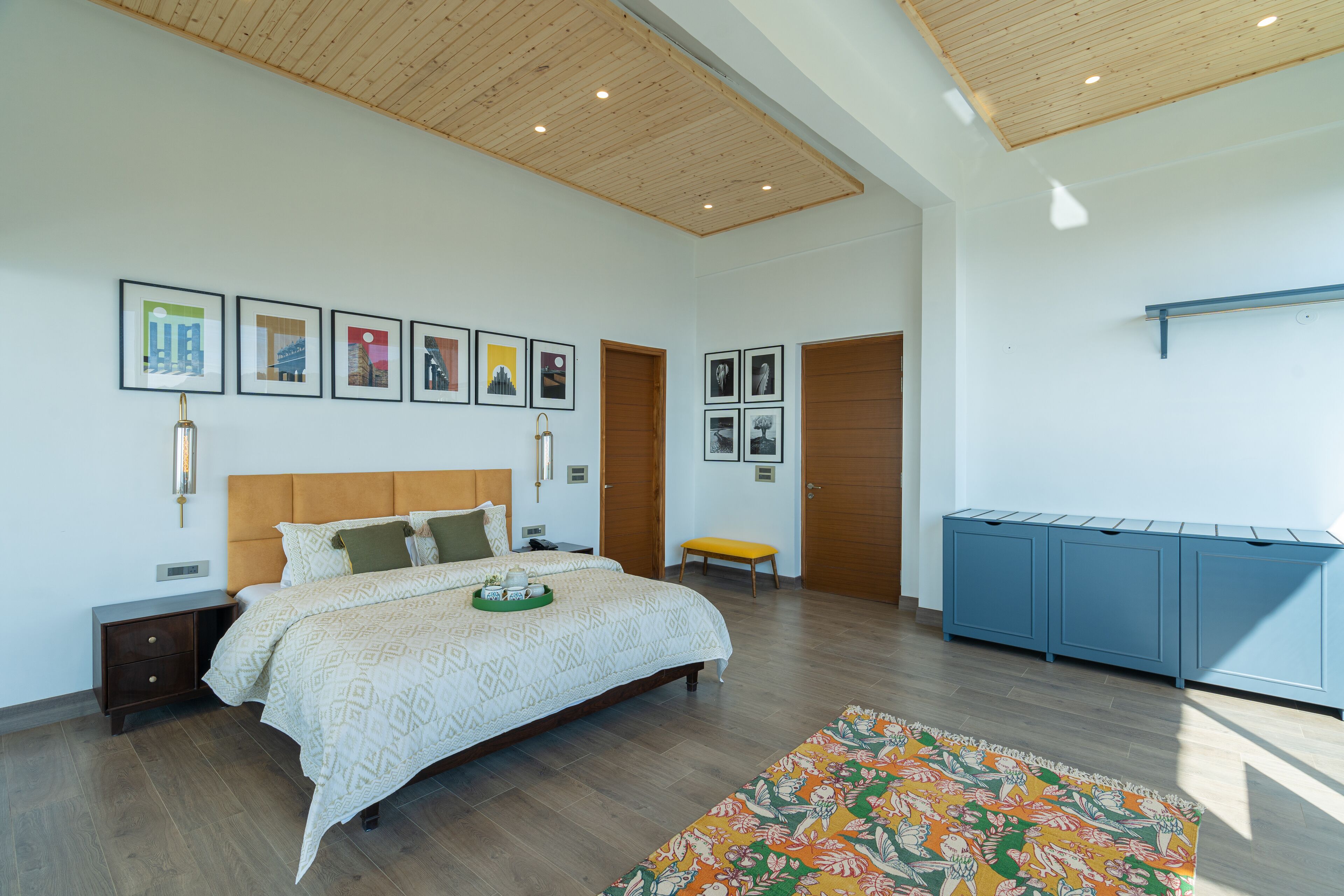Camera da letto moderna con soffitto in legno, un letto grande con biancheria a motivi, un comodino, una panca e un armadietto blu.