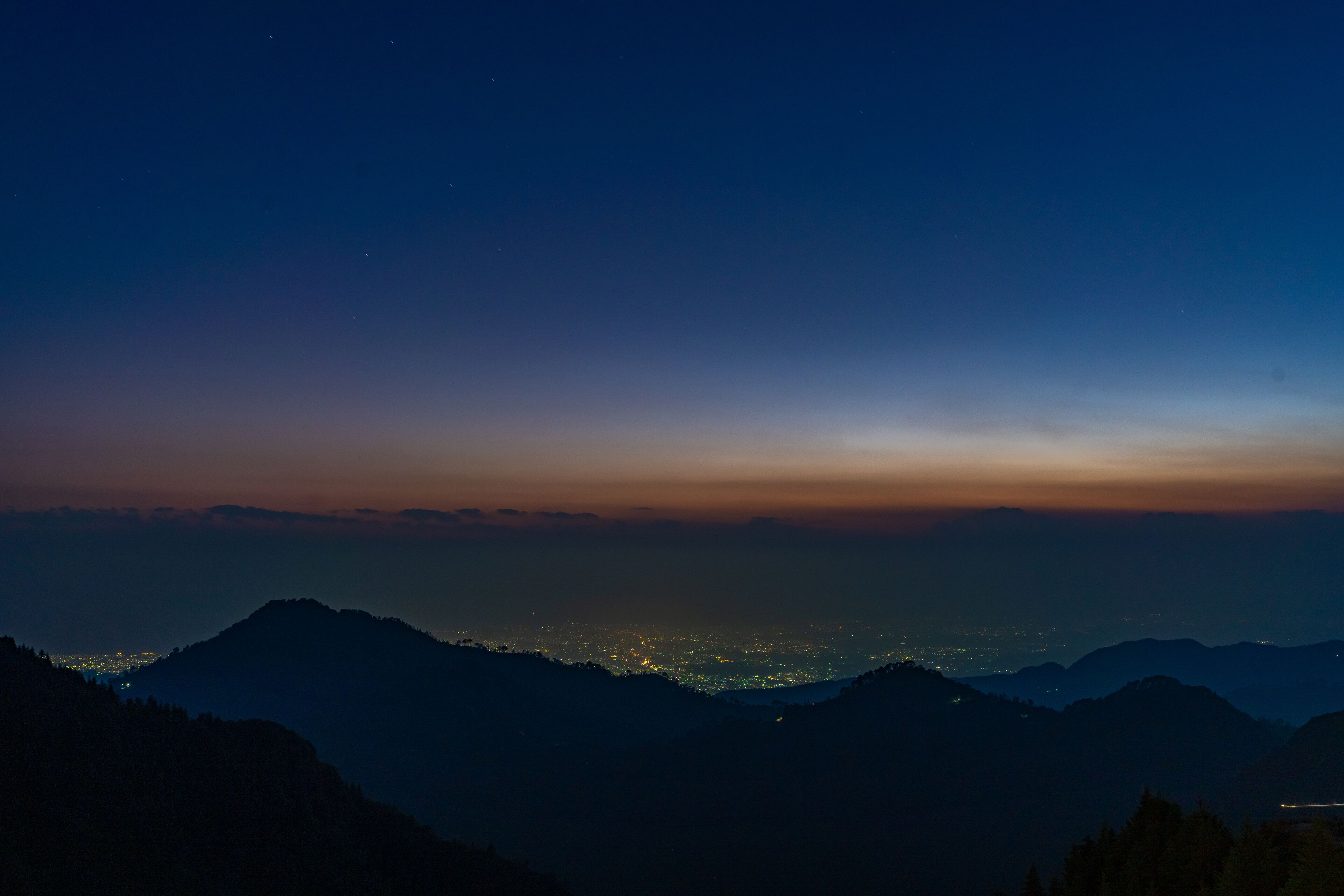 Une vue nocturne d’un paysage montagneux, avec les lumières de la ville qui scintillent au loin.