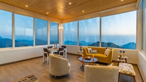 A spacious room with large windows offering a mountain view, a cozy seating area with a sofa and chairs, and a small table with candles. - Soul Stories - Luxury Villas and Resort, Mussorrie (Dhanaulti)