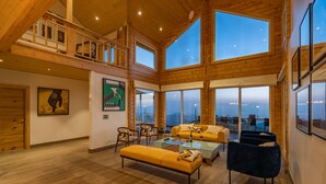 A spacious living area with wooden floors, a high ceiling, and large windows offering a view of the city. - Soul Stories - Luxury Villas and Resort, Mussorrie (Dhanaulti)