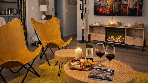 Un accogliente soggiorno con camino, una TV che mostra 'Stranger Things' e un tavolo apparecchiato con bicchieri da vino e formaggio.