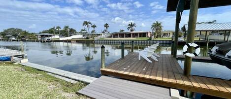 A wooden dock extending into a calm body of water, surrounded by a grassy area and palm trees.