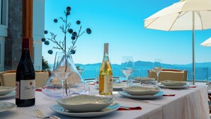 A table set for dining with wine bottles, glasses, and a decorative tree centerpiece, overlooking a scenic view. - Villa Valentino 1 (Bodrum)