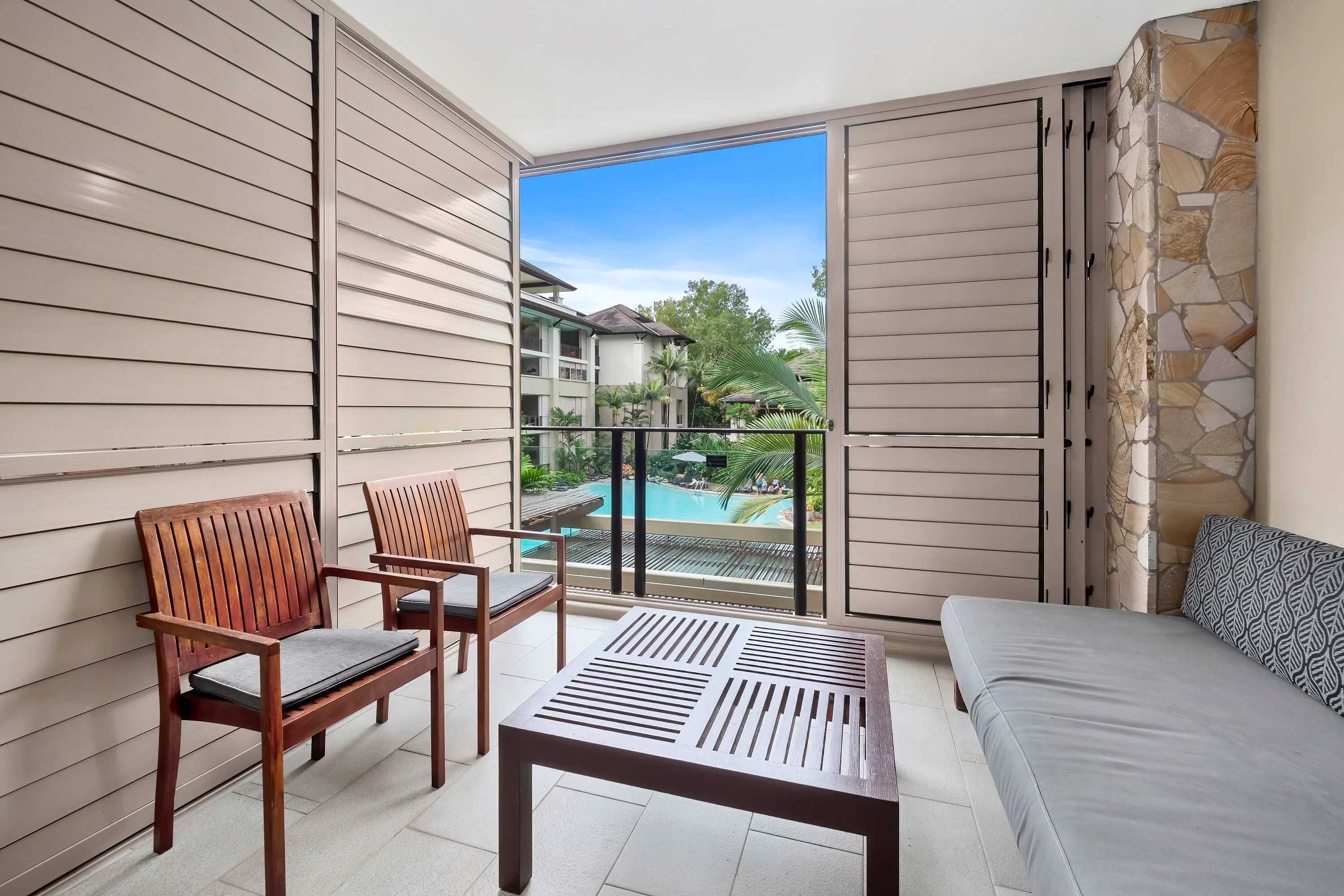 Un balcon avec vue sur la piscine, deux chaises en bois, un banc et un canapé.