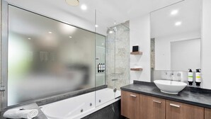 A modern bathroom with a glass-enclosed shower, a white bathtub, a large mirror, and a wooden vanity with a white sink.