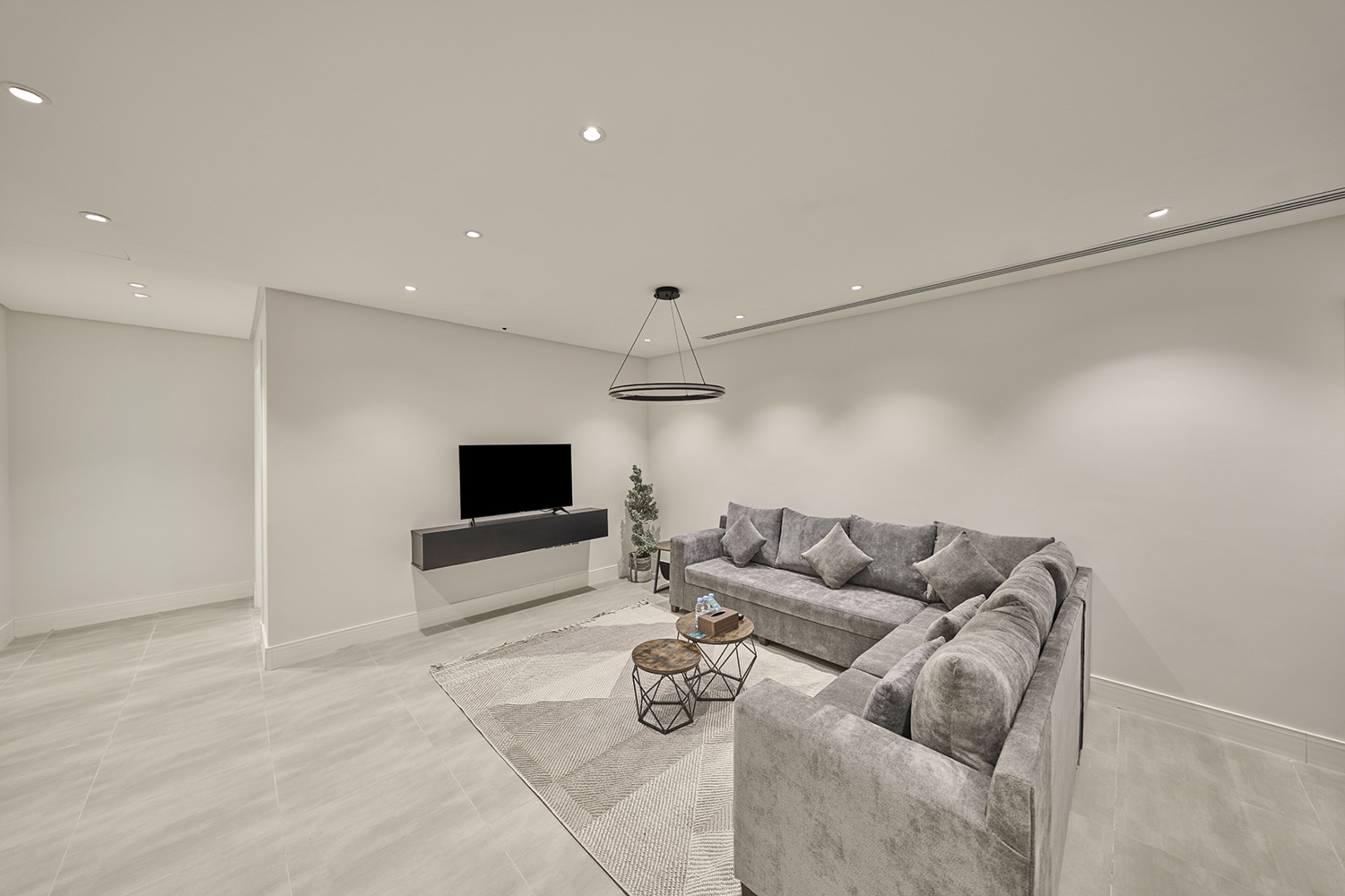 Una sala de estar moderna con un sofá gris, una mesa de centro y un televisor montado en la pared.
