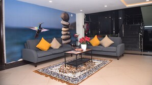 A modern lobby with a blue wall mural, a grey sofa with yellow cushions, a black coffee table, and a patterned rug. - M R RESIDENCY DHARWAD (Dharwad)