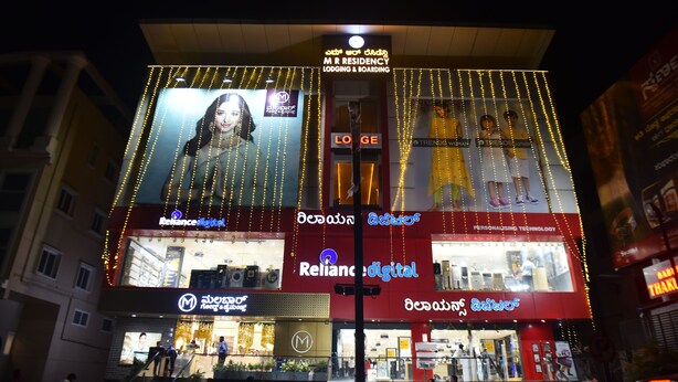 A building with multiple signs for M R RESIDENCY LODGING & BOARDING, Reliance Digital, and other businesses.