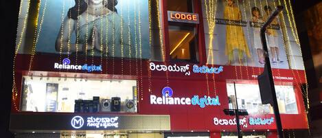 A building with a sign for 'M R Residency Lodging & Boarding' and 'Reliance Digital' store.