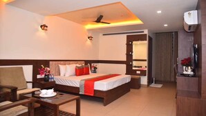 A hotel room with a bed, a desk, a chair, a bedside table, and a mirror. - M R RESIDENCY DHARWAD (Dharwad)