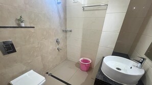A bathroom with a toilet, sink, shower, and a small shelf with a plant. - M R RESIDENCY DHARWAD (Dharwad)